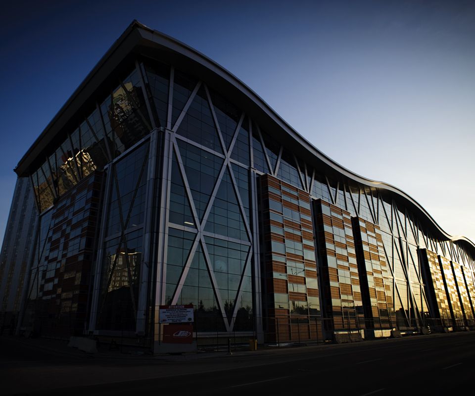 A modern glass-and-steel building with a curved roof and large diagonal support beams.