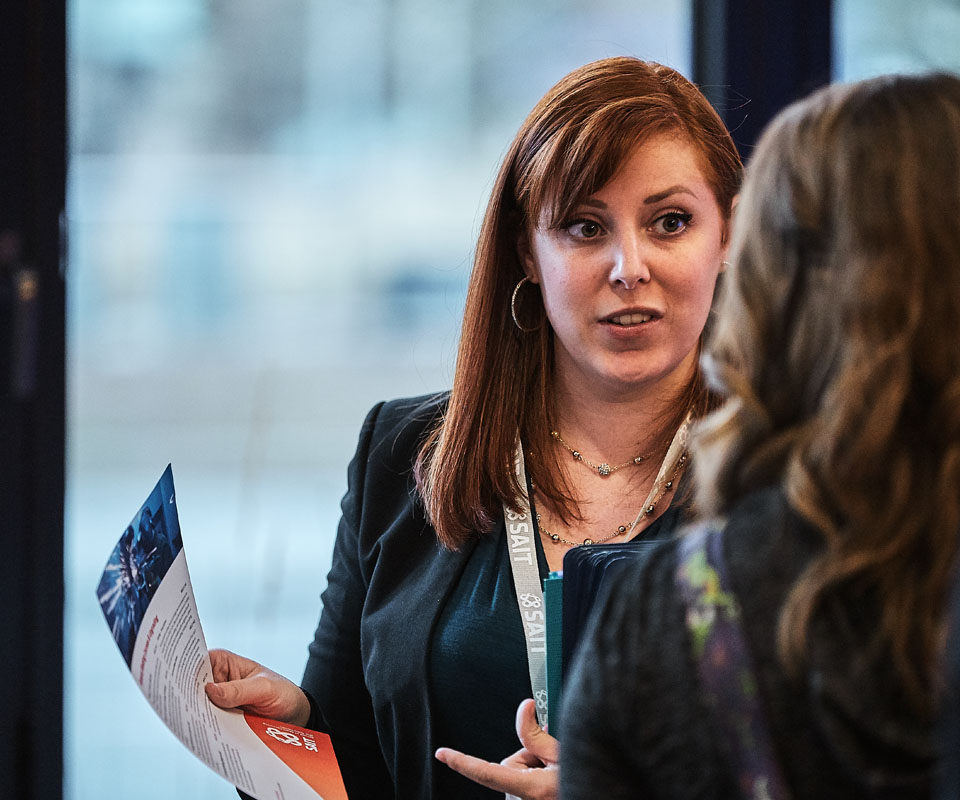An advisor with red hair speaks to a prospective student while holding an informational brochure.