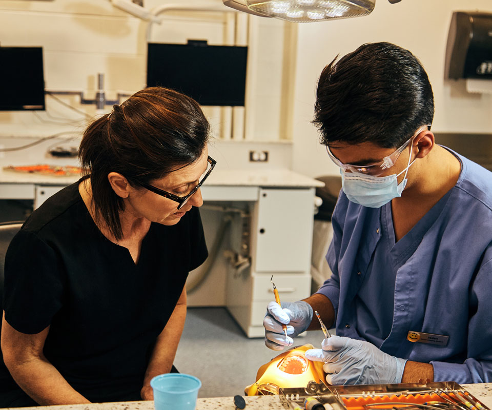 A dental assistant student practices a procedure on a dental model while an instructor watches attentively.