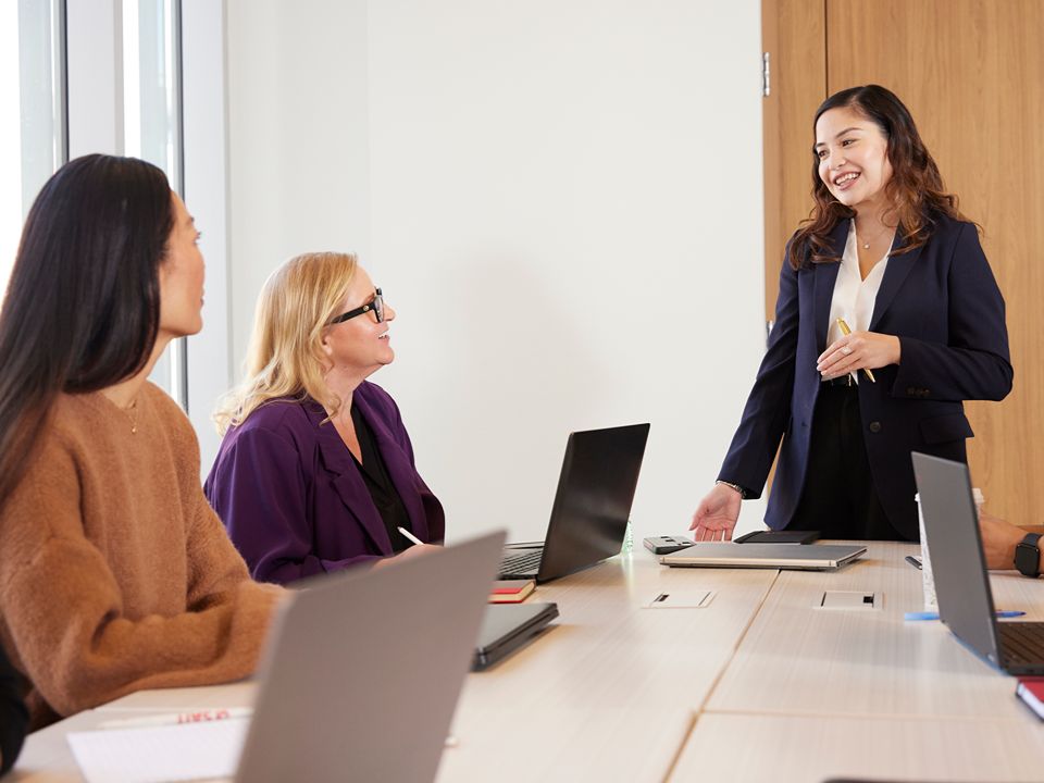 Four colleagues in a meeting room, with one presenting to the group