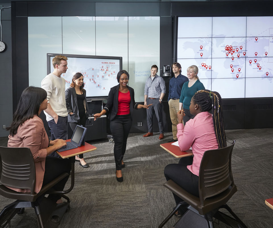 Group of diverse professionals collaborating in a modern conference room with digital displays showing global data.