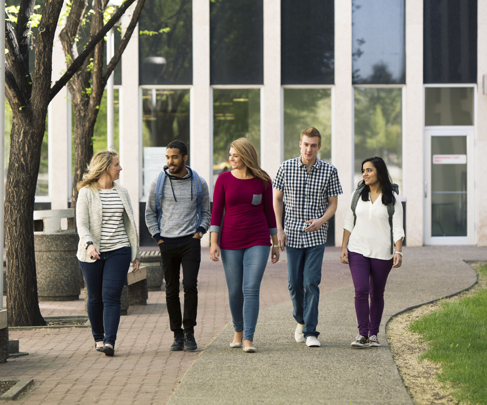 A diverse group of five college students walking together outside the Senator Burns Building main entrance.