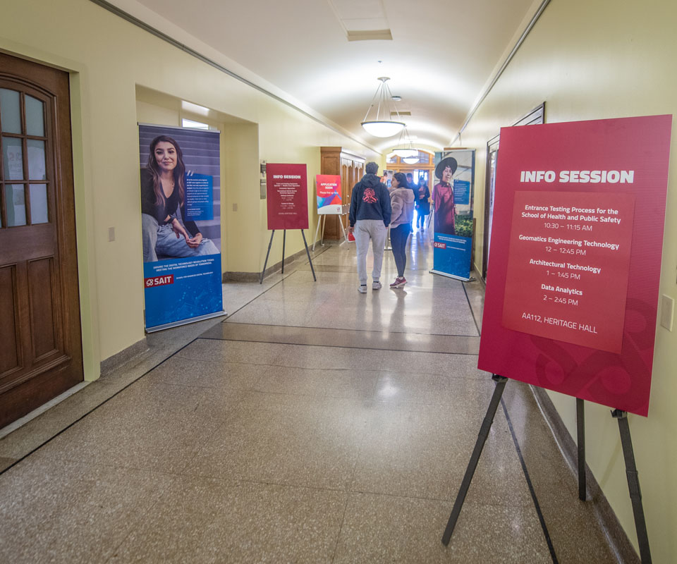 A hallway with posters and signs promoting SAIT information sessions.