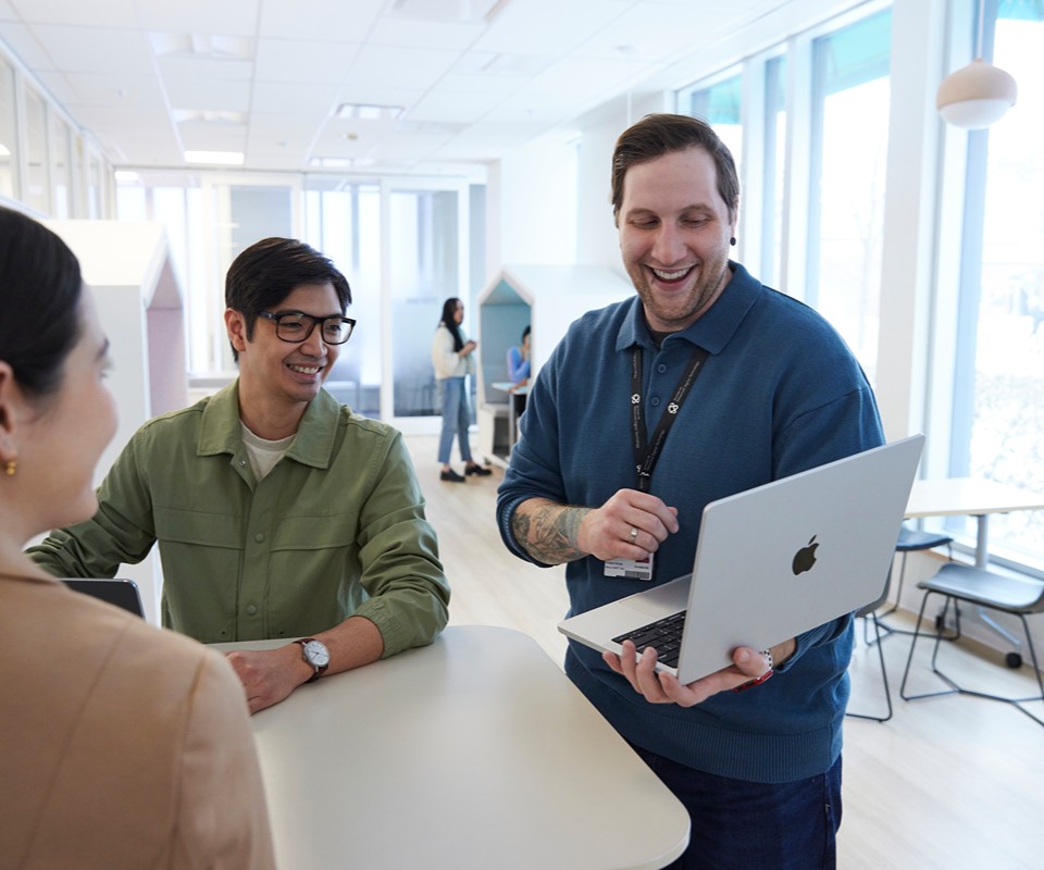 An instructor holding their laptop is smiling and showing students the screen.