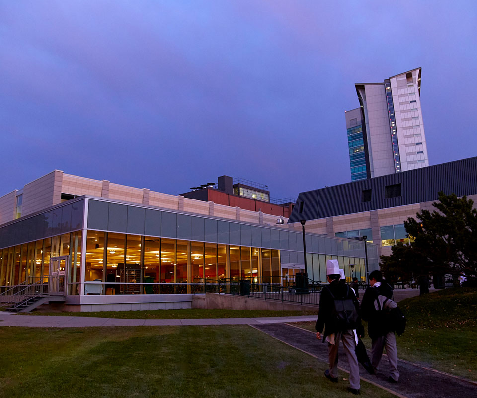 Students walking past the John Ware Building at dusk, showcasing a blend of glass and architecture.