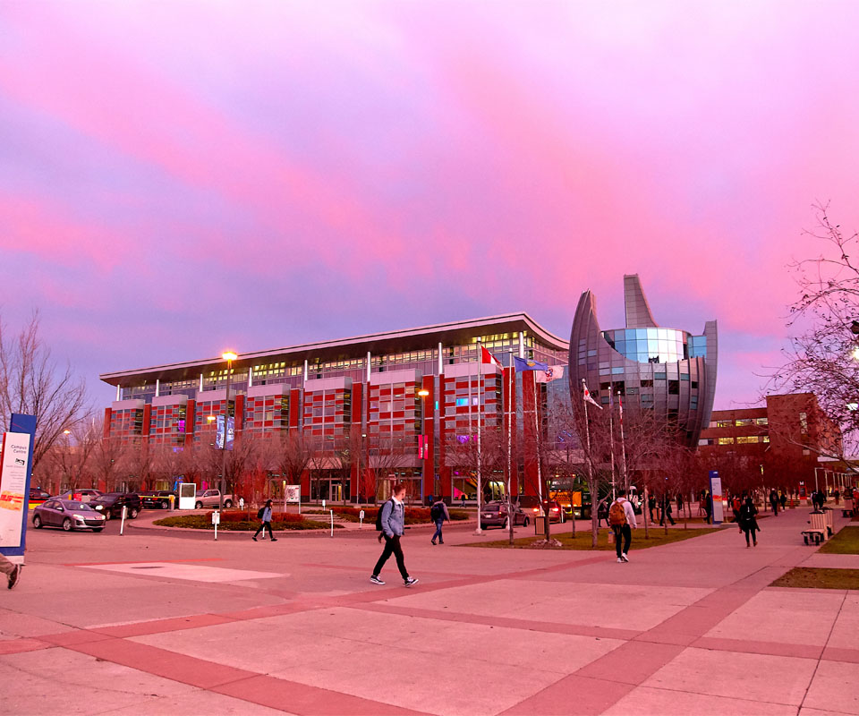 The modern exterior of the Johnson-Cobbe Energy Centre with colorful glass panels under a pink sky at dusk.