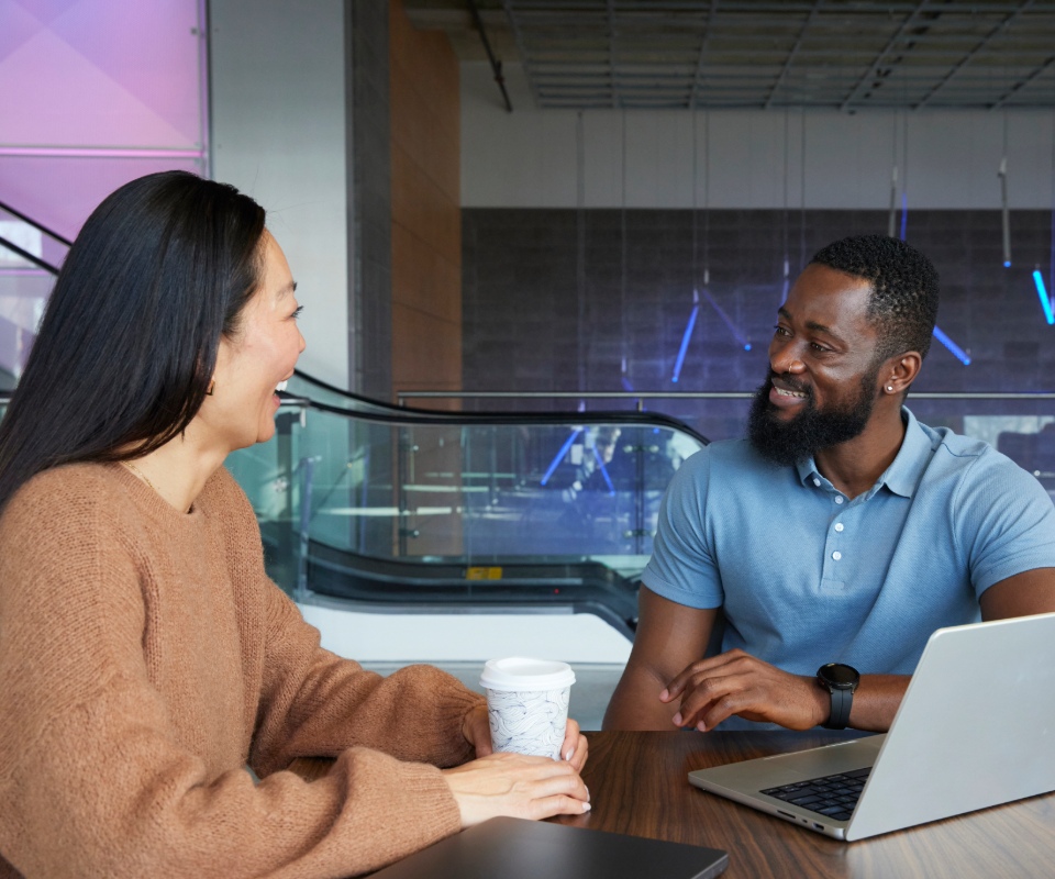 A smiling man engaged in conversation with a woman at a modern workspace, showcasing a collaborative environment.