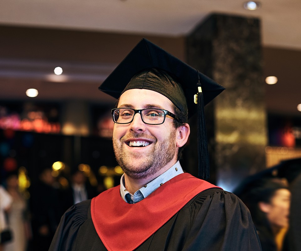 A smiling graduate wearing a cap and gown, showcasing happiness and achievement at a graduation event.
