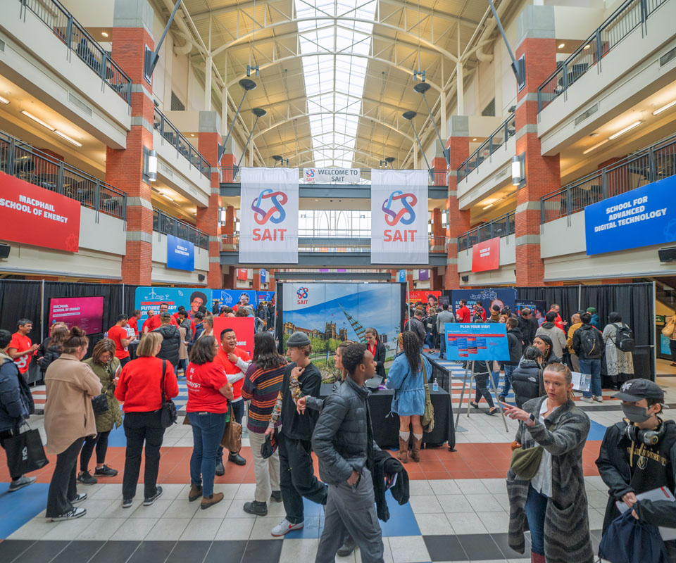 A vibrant Open House info fair scene at SAIT showcasing various booths and banners, with attendees engaging in conversations and activities.
