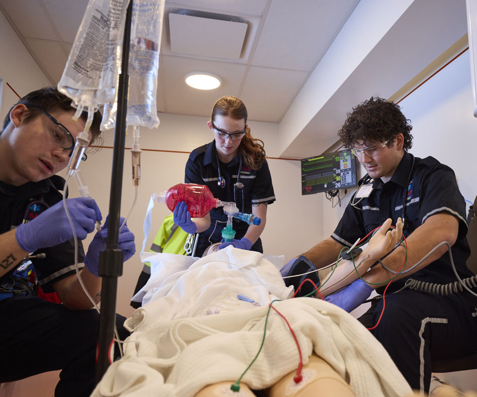 Emergency medical personnel providing care to a simulated patient in a medical training scenario.