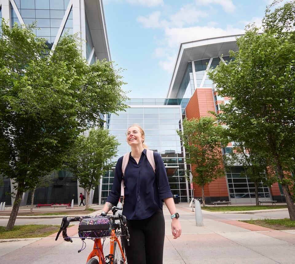 Women walking on campus with a bike while wearing a backpack