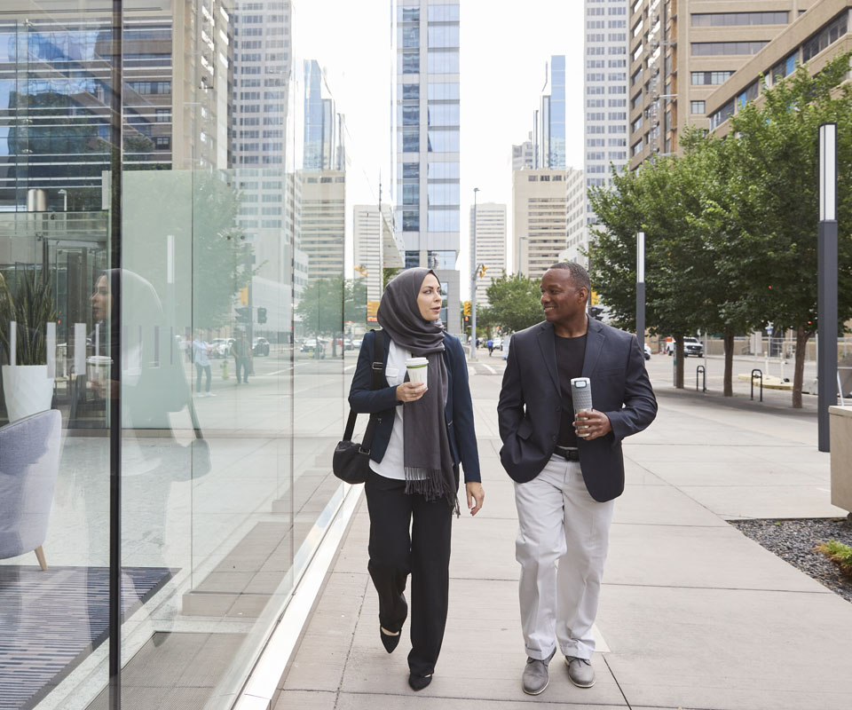 A diverse professional pair walking and chatting along a street in downtown Calgary, reflecting a modern urban environment.