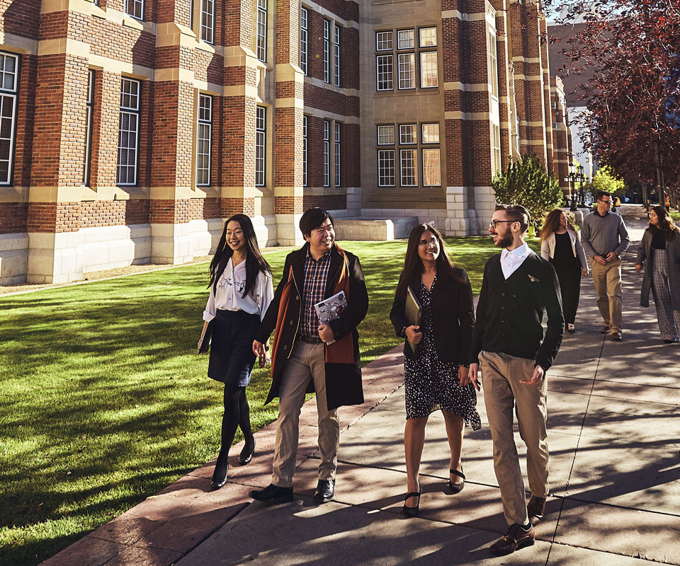 A group of diverse students walking together on campus, smiling and engaging with one another. Heritage Hall and lush green lawn create a vibrant academic atmosphere.