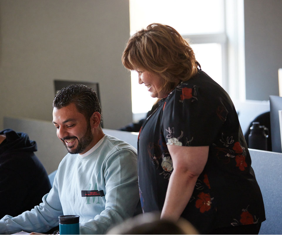 A SAIT instructor engaging with a student in a discussion while seated at a desk in an office environment.