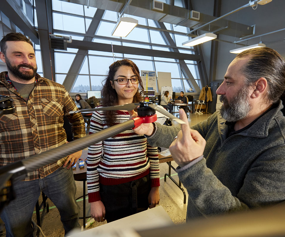 Three individuals collaborating on a drone project, focusing on a drone's rotor while discussing its features.