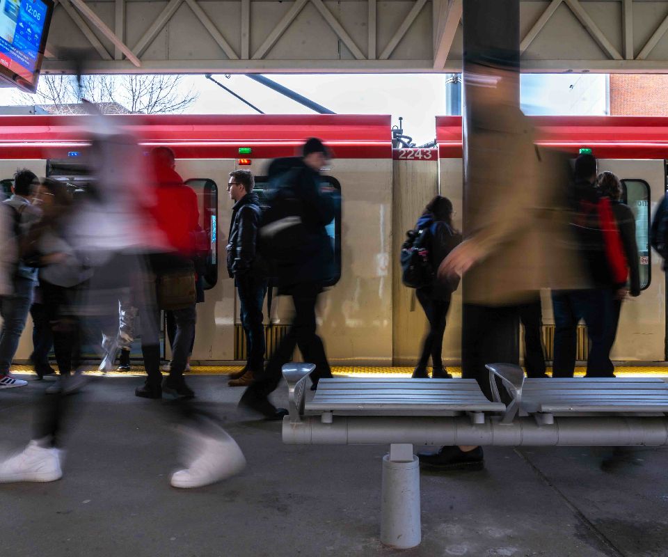 A bustling train station scene featuring a train arriving as commuters rush to board. The motion blur captures the energy and movement of the crowd.
