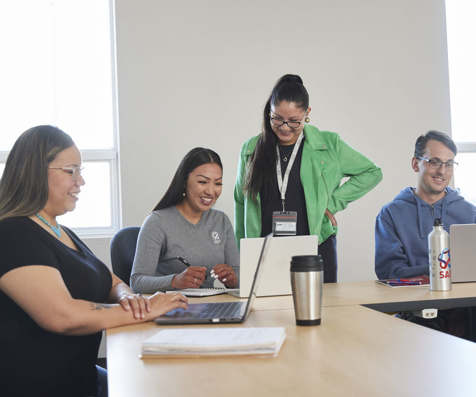 Group of four people collaborating at a table with laptops and notebooks in a bright, modern workspace.