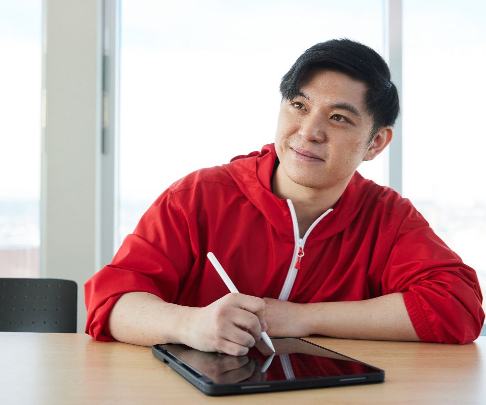 student in red taking notes on a tablet