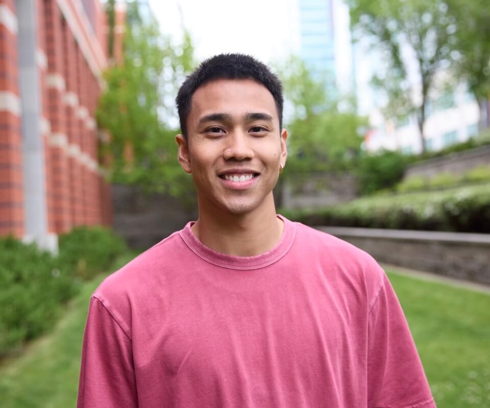 A student wearing a pink shirt looks right at the camera