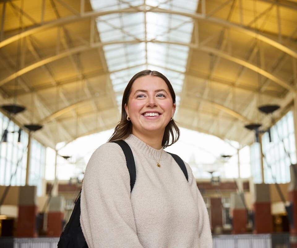 A student standing inside a building smiles looking over the camera