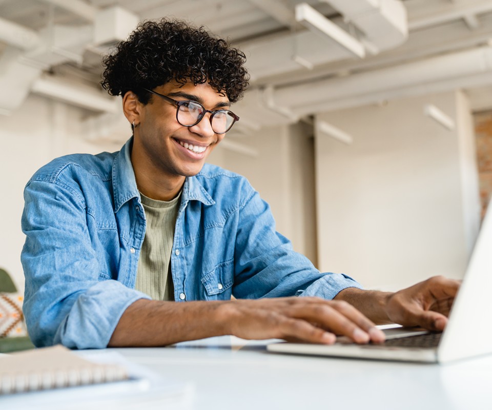 A student scrolls on his computer, smiling at the screen.