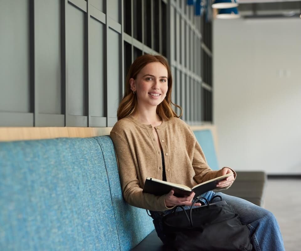 A female student sits on a bench looking at the camera