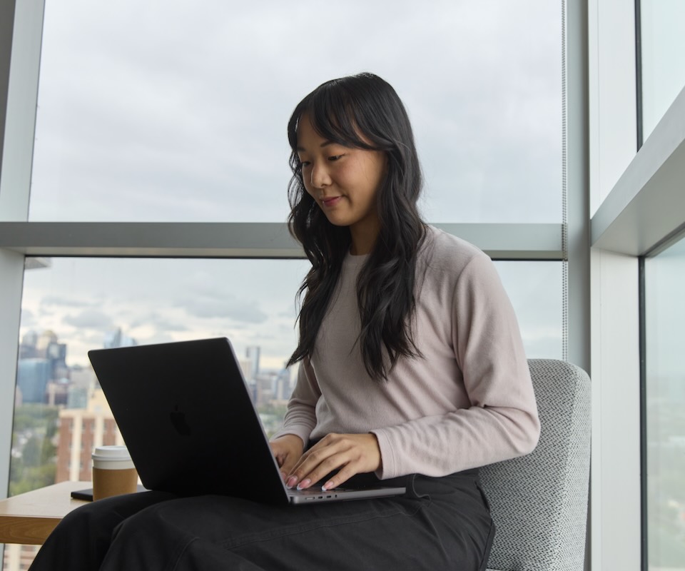 A woman works on a laptop with a cup of coffee beside her.
