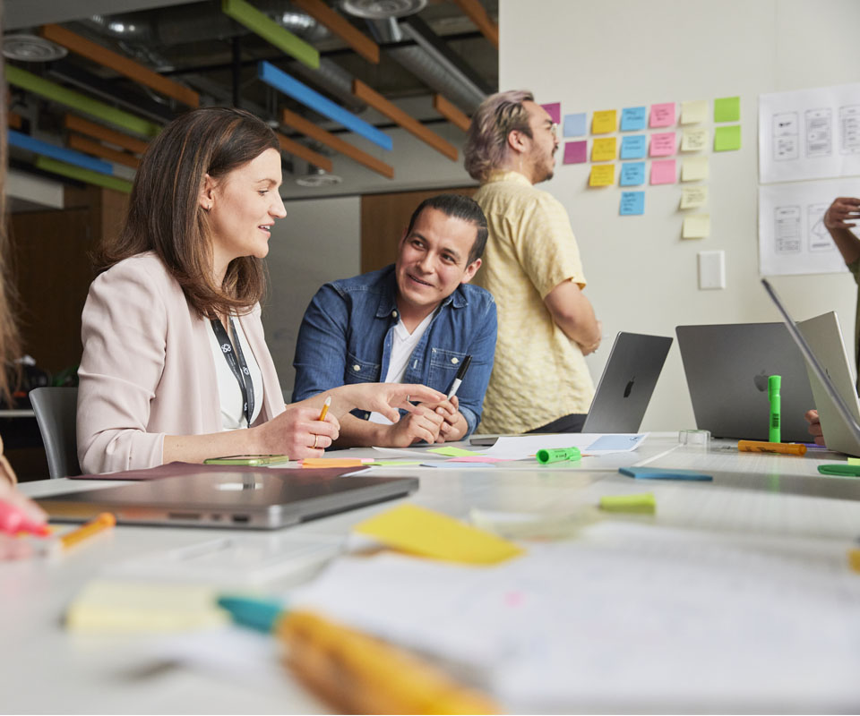 A collaborative brainstorming session between students discussing ideas around a table filled with colourful sticky notes and laptops.