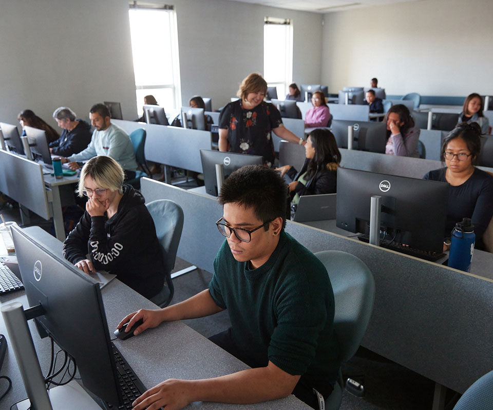 Students engaged in focused work on computers inside a classroom setting.