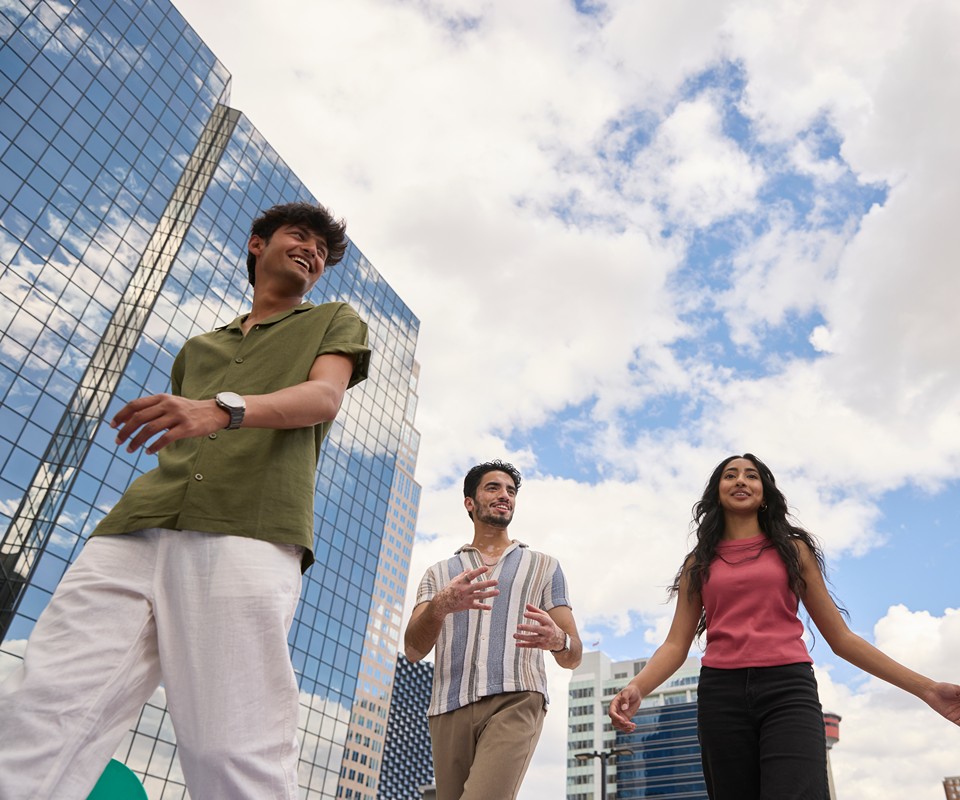 Three young adults walking outdoors in an urban setting with modern buildings and a blue sky.