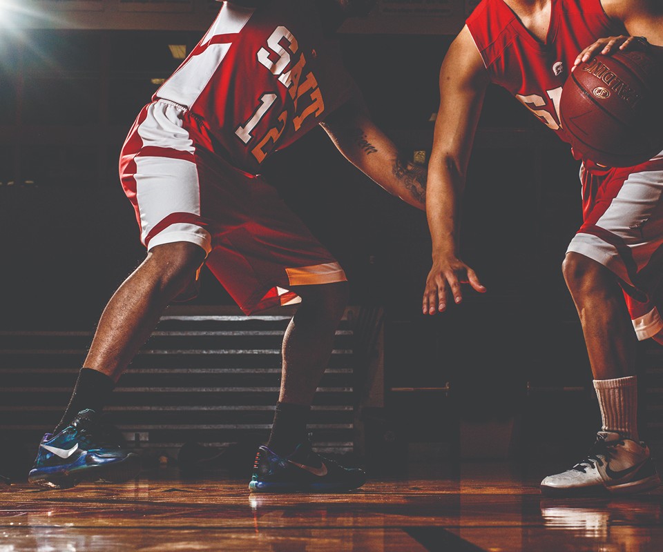 Two basketball players in red uniforms engage in a dynamic dribbling maneuver on the court.