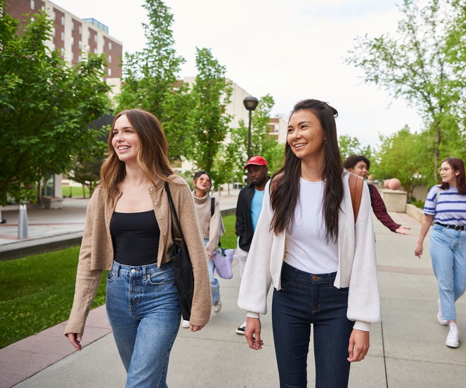 A group of diverse young adults walking together on a campus, smiling and enjoying each other's company.