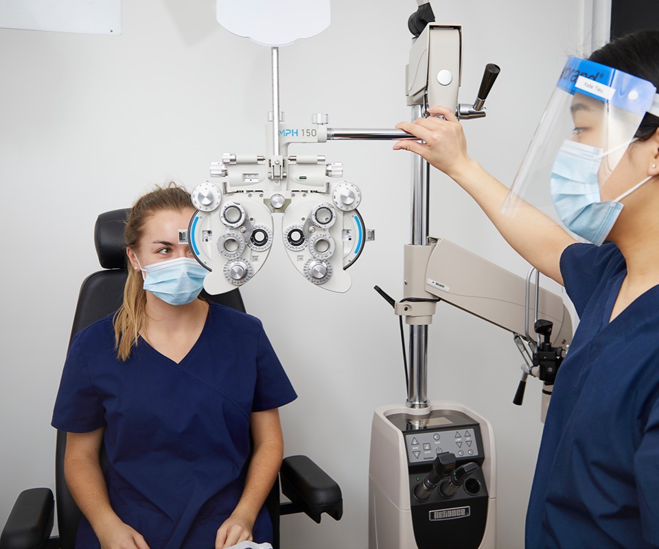 A healthcare professional conducts an eye examination on a patient using a phoropter and other optometric equipment.