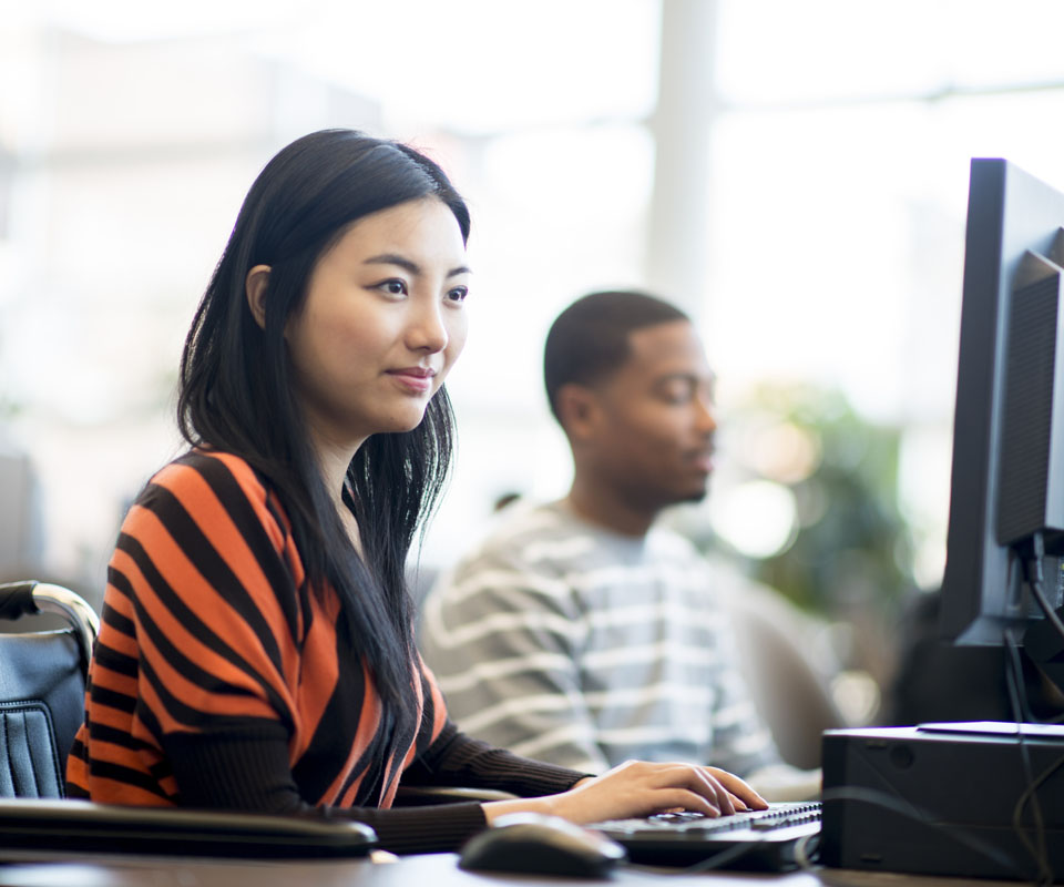 A woman in a wheelchair focuses on her computer screen while a man works at a nearby desk in a bright, modern office setting.