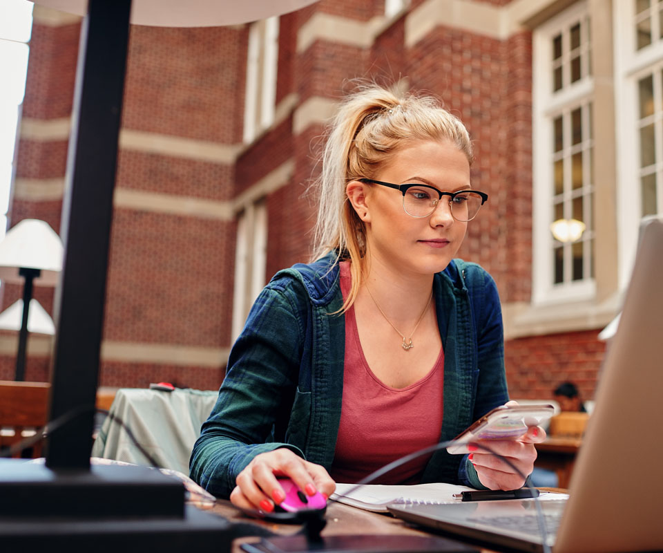 A student using a laptop and smartphone while studying in Heritage Hall.