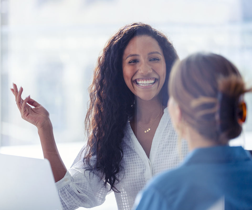 A smiling woman engaging in a friendly conversation with another person in a professional setting.