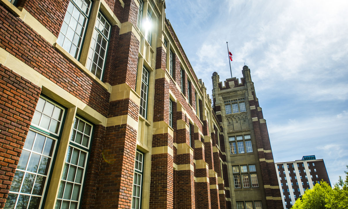 Historic brick school building with a flag atop its tower and a clear blue sky in the background.