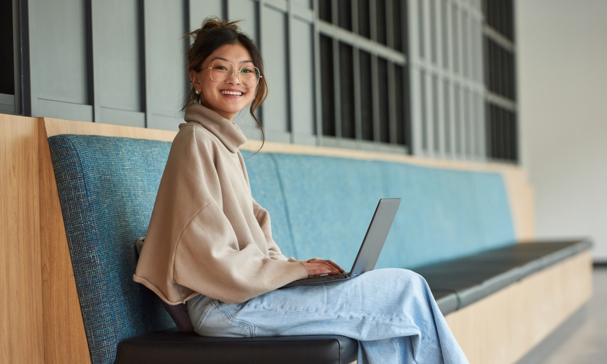 A student is seated with a laptop, smiling.