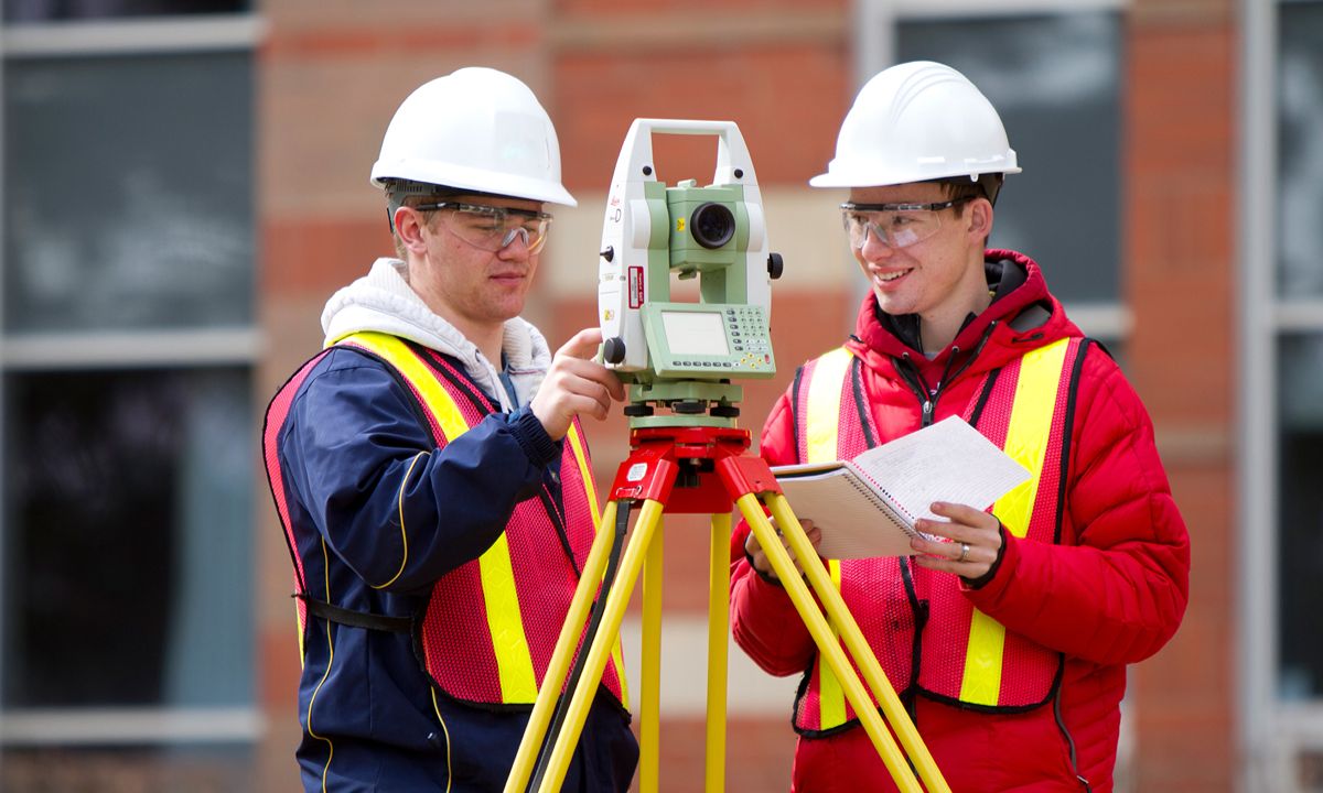 surveyors using tripod instrument outside brick building