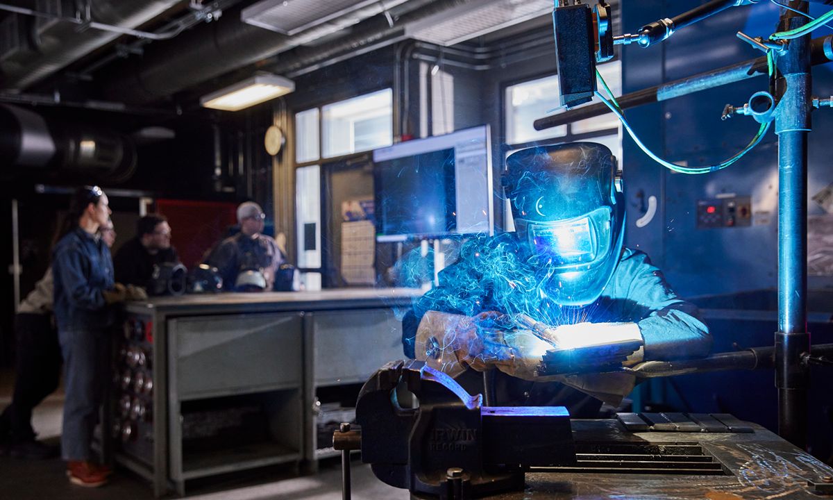 welder working with sparks in shop while others observe