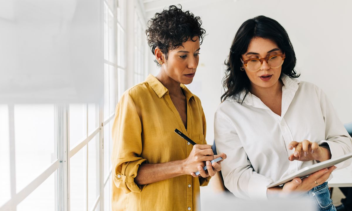 woman pointing at tablet other taking notes