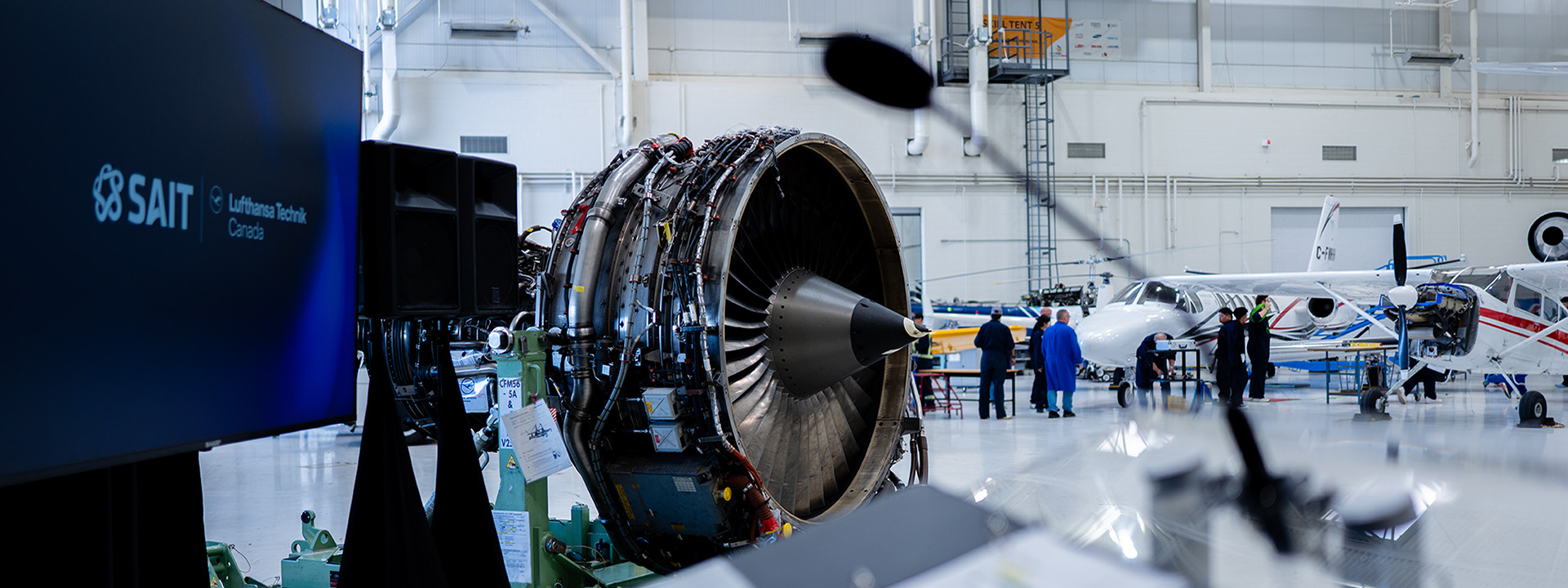 A smiling woman with long brown hair stands in front of a colorful graffiti mural and modern skyscrapers.