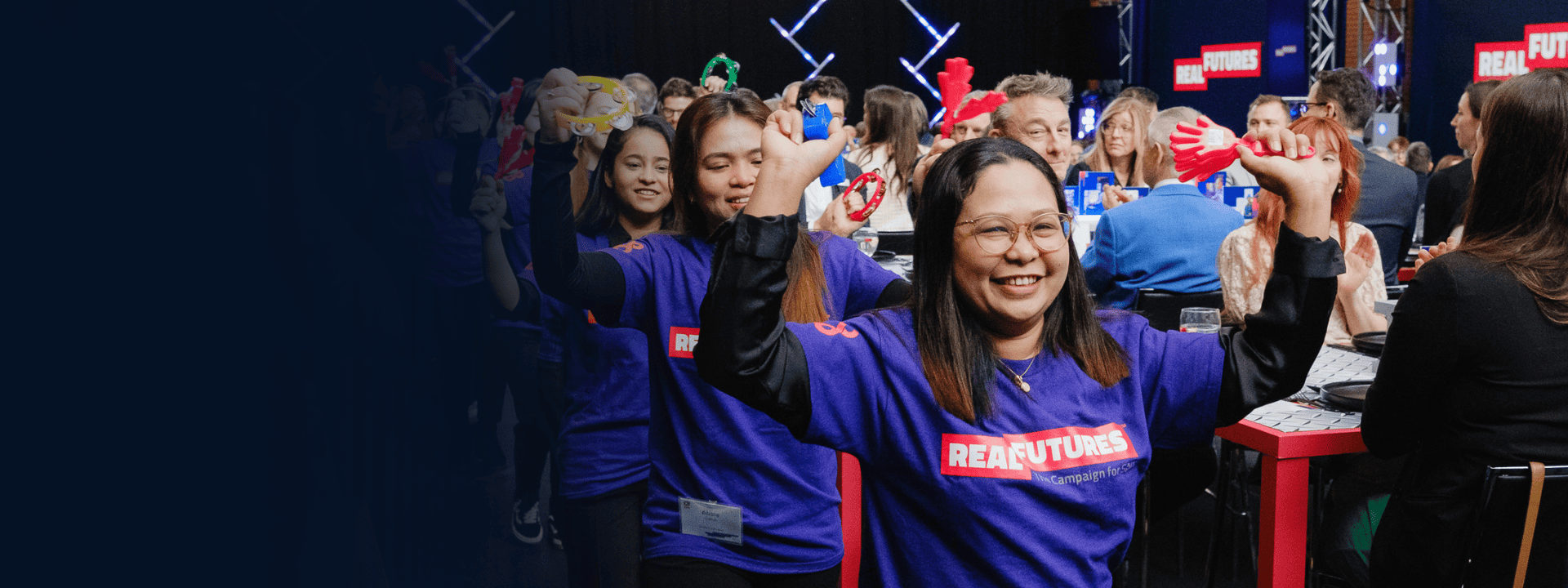 Participants at a conference enthusiastically engaging in an interactive activity, wearing matching purple shirts with REAFUTURES displayed.