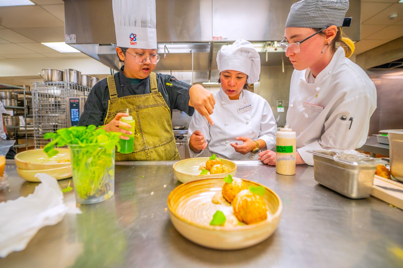 A chef teaching two students in a kitchen
