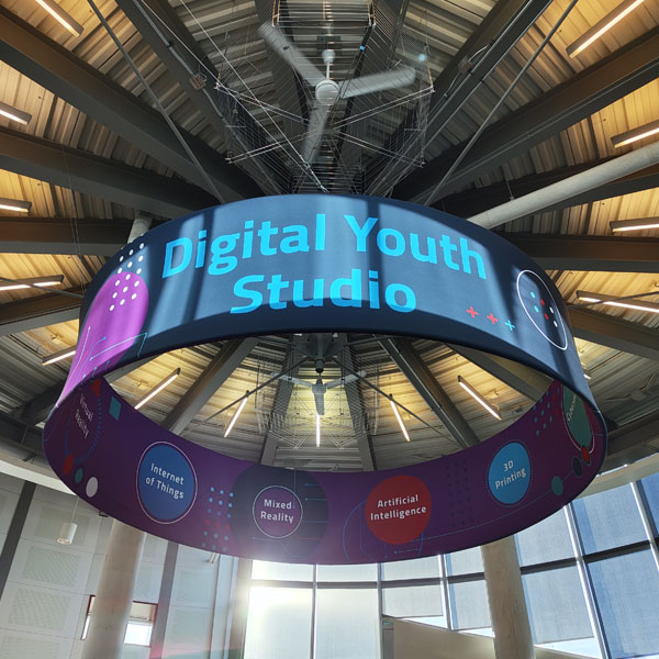 A large circular hanging banner reads Digital Youth Studio featuring colourful sections labeled with technology topics like Internet of Things, Mixed Reality, Artificial Intelligence, and 3D Printing.