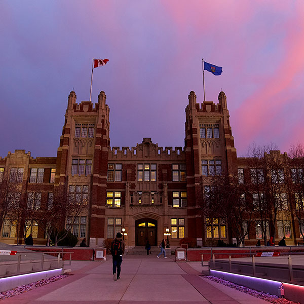 Modern glass building with a wavy roofline illuminated by purple lights at dusk.