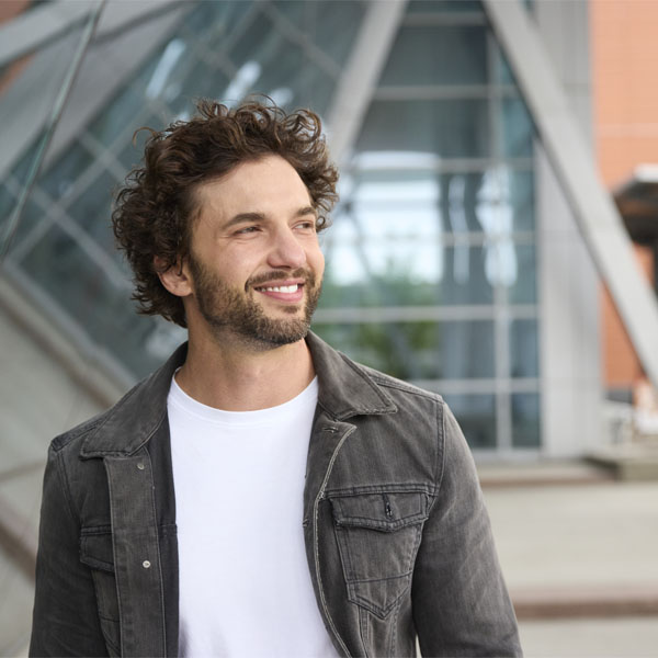 A smiling man with curly hair wearing a casual jacket stands outside the Johnson Cobbe Energy Centre main entrance.