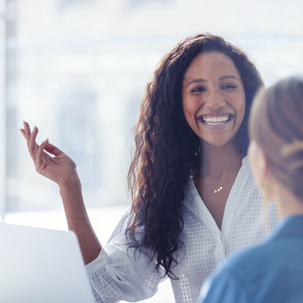 A smiling woman in a professional setting engaged in conversation with another person.