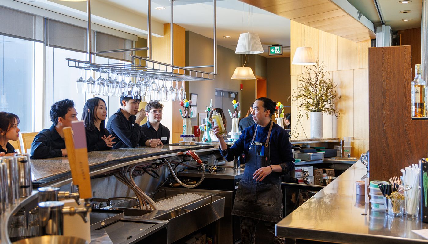 A group of individuals stands on one side of a modern bar counter while an instructor works behind the counter.