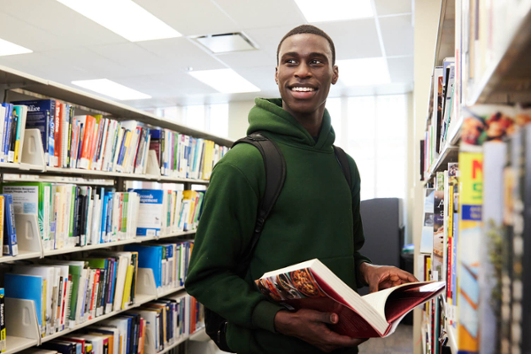 A student in a library with book shelves surrounding him